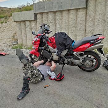 Man traveller repairing his motorbike on road lying on asphalt