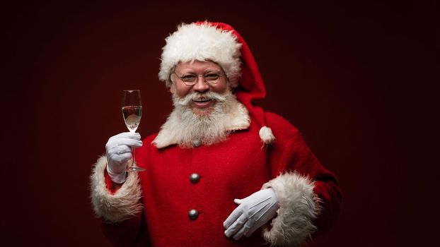 Santa Claus holding glass of champagne and smiling, closeup portrait isolated on dark Background