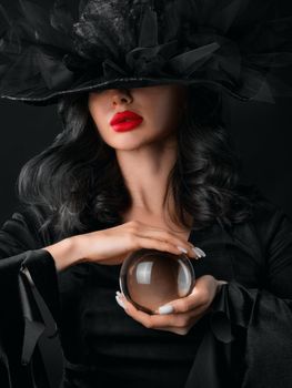 Woman in Halloween witch fortune teller costume with crystal ball. Beautiful sexy model girl in sinister costume and make up