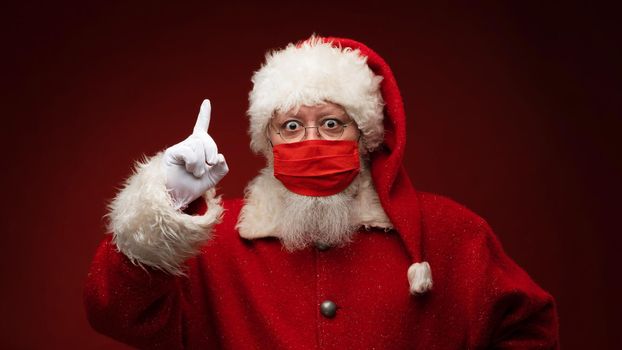 Santa Claus in red medical mask pointing finger up restriction covid christmas celebration concept