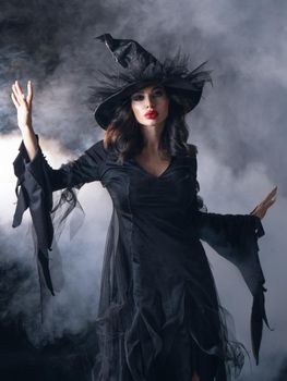 Sexy young brunette witch with put a spell in mist Halloween party costume
