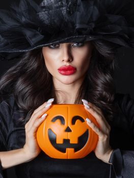 Woman in witch costume hold Halloween pumpkin bucket for candies close up beauty portrait