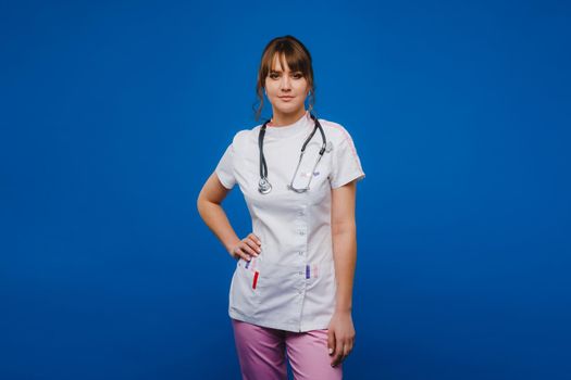 A female doctor, gesticulating, checks the heartbeat in the doctor's office at the hospital with a stethoscope isolated on a blue background.