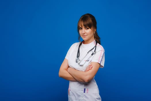 A female doctor, gesticulating, checks the heartbeat in the doctor's office at the hospital with a stethoscope isolated on a blue background.