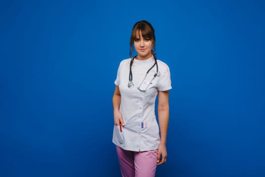 A female doctor, gesticulating, checks the heartbeat in the doctor's office at the hospital with a stethoscope isolated on a blue background.