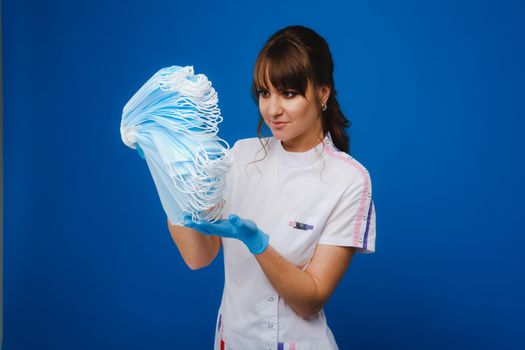 the doctor is holding a bunch of medical masks stacked together on a blue isolated background.