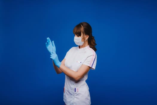 A doctor girl stands in a medical mask on an isolated blue background