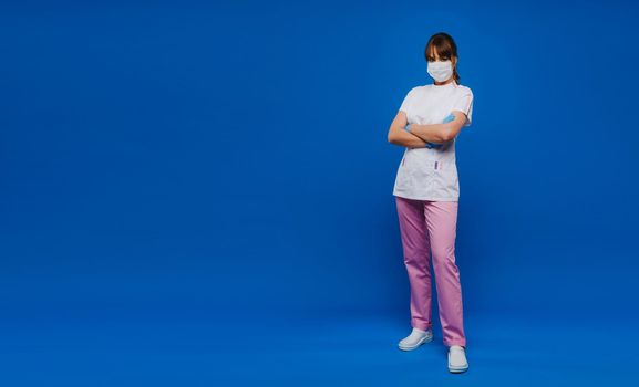 A girl doctor stands in a medical mask and gloves on an isolated blue background.