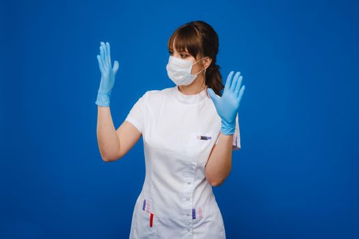 A girl doctor stands in a medical mask and gloves on an isolated blue background.