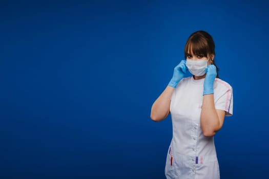 A doctor girl stands in a medical mask on an isolated blue background