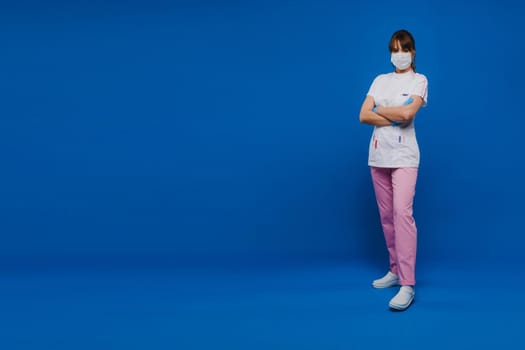 A girl doctor stands in a medical mask and gloves on an isolated blue background.