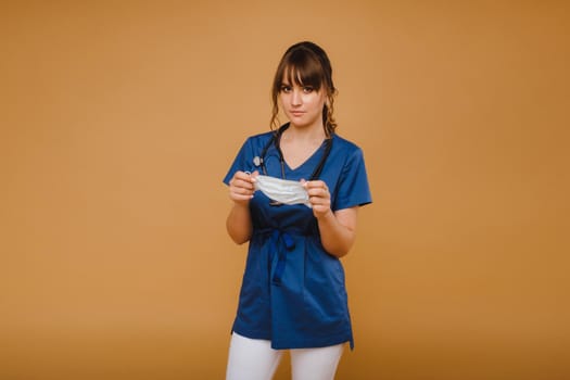 A girl doctor stands in a medical mask, isolated on a brown background.