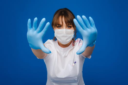 A girl doctor stands in a medical mask and gloves on an isolated blue background.