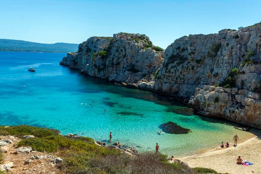 Marathopoli, Greece - August29, 2019: People swimming in the clear blue waters of Proti Island, near Marathopoli, Messinia at Peloponnese. The name of the island derives from the ancient sea god Proteus, son of Poseidon.