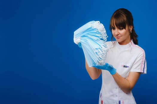 the doctor is holding a bunch of medical masks stacked together on a blue isolated background.