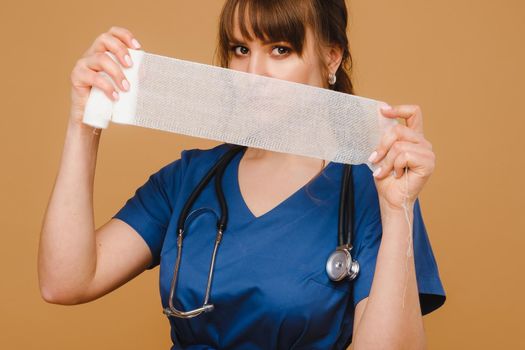 a female doctor in a white coat holds twisted gauze bandages for dressing wounds on a brown background.