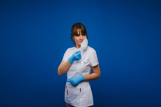 A doctor girl stands in a medical mask on an isolated blue background