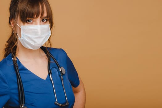 A girl doctor stands in a medical mask, isolated on a brown background.