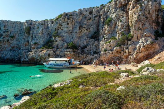 Marathopoli, Greece - August29, 2019: People swimming in the clear blue waters of Proti Island, near Marathopoli, Messinia at Peloponnese. The name of the island derives from the ancient sea god Proteus, son of Poseidon.