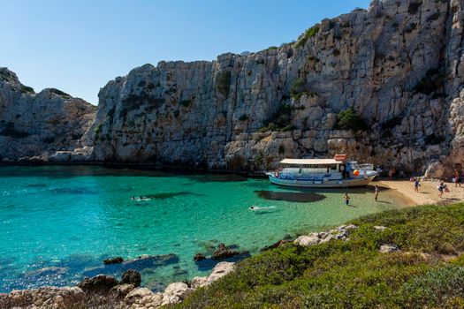 Marathopoli, Greece - August29, 2019: People swimming in the clear blue waters of Proti Island, near Marathopoli, Messinia at Peloponnese. The name of the island derives from the ancient sea god Proteus, son of Poseidon.