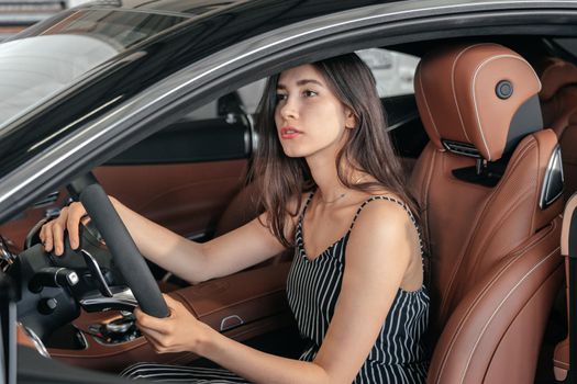 Young asian woman sitting in luxury car in garage before starting engine and driving