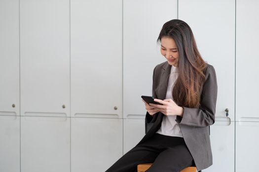 Cheerful working woman using mobile phone smiling with pleasure as she reads a text message in office.