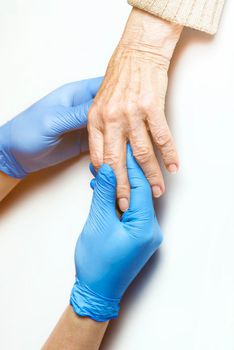 Doctor's hands in a blue gloves holds the hands of an elderly woman, a patient. Handshake, caring, trust and support. Medicine and healthcare.