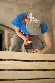 Ukraine, Goshcha, voluntary event, - August, 2021 - skilled young female worker is using power screwdriver drilling during construction wooden bench, gender equality, feminism