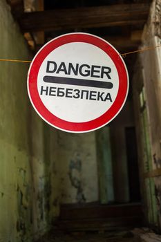 Old wrecked house with 'Danger' in English and in Ukrainian warning sign, abandoned building, uninhabitable place.