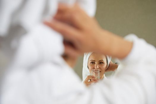 Beautiful happy girl drinking and holding glass of water standing in front of mirror in the morning. Concept of healthy lifestyle