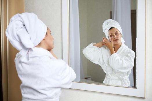 Young woman with hair wrapped in towel near mirror indoors