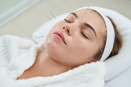 Young woman having an acupuncture treatment therapy on face in spa salon. Alternative medicine and therapy concept