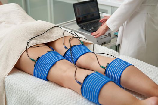 The procedure of myostimulation on legs of a woman in a beauty salon. Caring for the body with electrostimulation