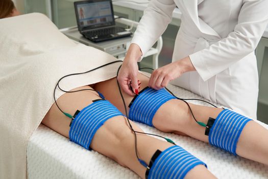 The procedure of myostimulation on legs of a woman in a beauty salon. Caring for the body with electrostimulation