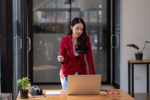 Charming asian businesswoman standing working on laptop in office.