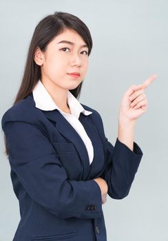 Asian businesswoman in suit with finger pointing up on gray background