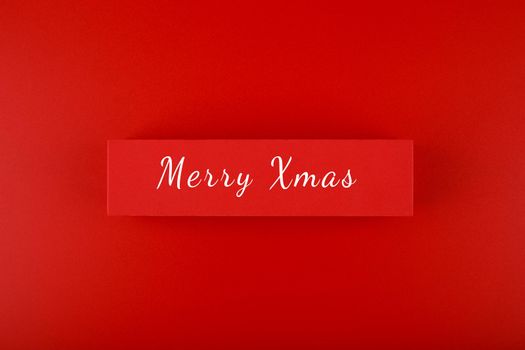 Minimal elegant flat lay Christmas theme. Merry Christmas text hand written on red tablet on red background. Creative layout in red colors