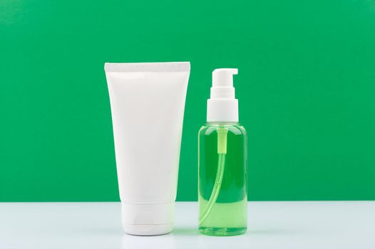 Cosmetic set with face cream or lotion and cleansing foam or gel in transparent bottle with dispenser on white table against green background. Concept of organic natural beauty products