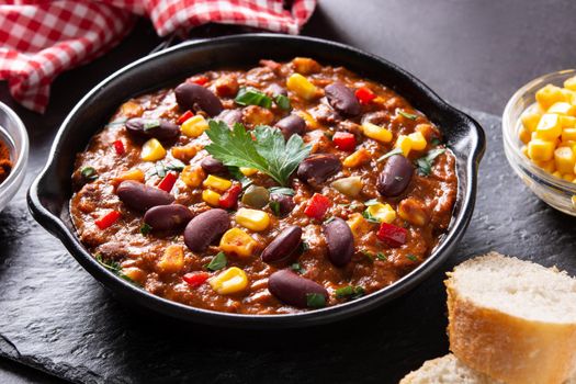 Traditional mexican tex mex chili con carne in iron pan on black background