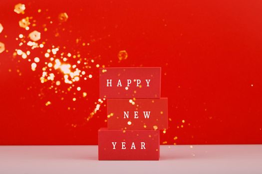 Happy New Year red minimal trendy concept. Modern festive composition with red toy blocks with written Happy New Year text against red background with golden bokeh