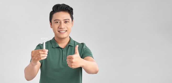 Young asian man holding a razor blade smiling and raising thumb up