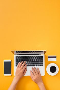 Businesswoman working is typing on computer keyboard with mobile, credit card and coffee cup on color background