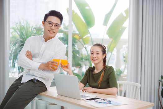 Happy young couple holding glasses of orange juice at the living room and looking to each othe