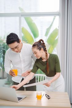 Adorable smiling couple bonding while working and drinking orange juice in bright warm sunny day