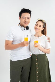 Stylish couple in casual clothes is drinking juice, looking at camera and smiling on white background