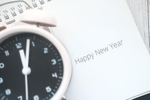 happy new year text on calendar with clock on table .