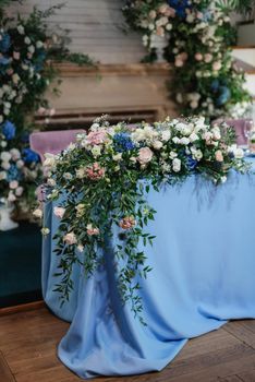 The presidium of the newlyweds in the banquet hall of the restaurant is decorated with candles and green plants, wisteria hangs from the ceiling