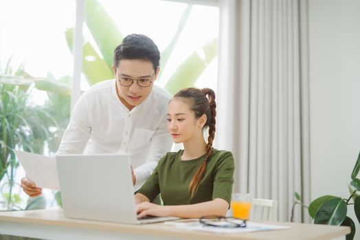 Wide shot of smiling couple surfing in laptop sitting at table