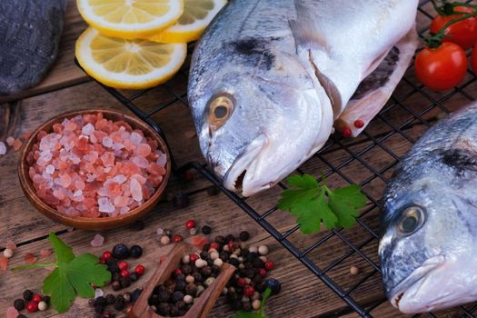 Fresh fish dorado. Raw dorado with salt, pepper, herbs, spices and lemon slices ready to cook on a wooden background. Top view.