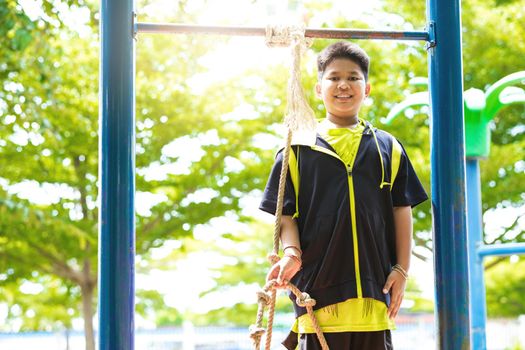 Young asian boy hang the yellow bar by his hand to exercise at out door playground under the big tree